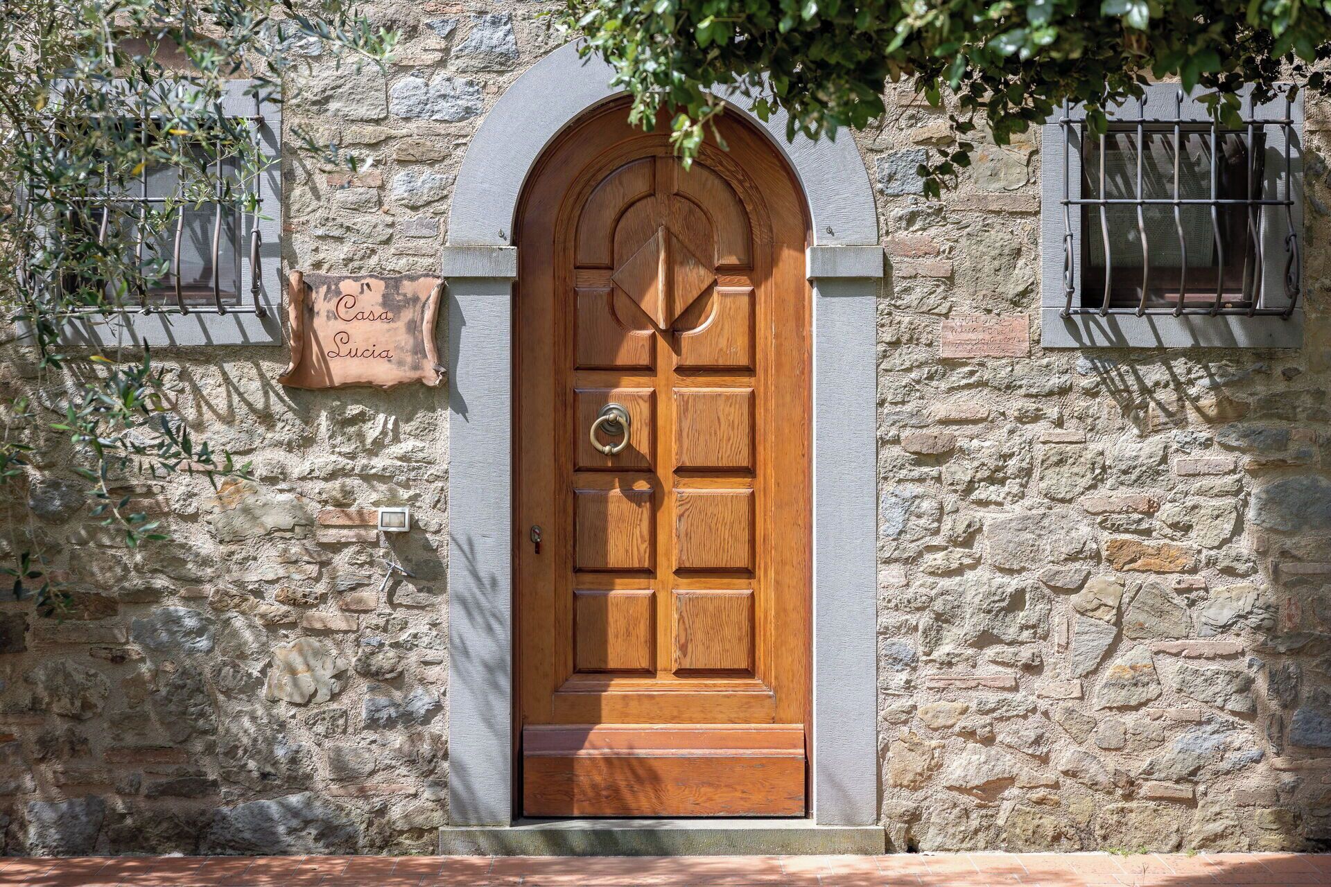 Un edificio de piedra con puerta de madera, una pequeña placa y una ventana con barrotes.