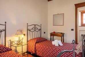 Ein Schlafzimmer mit einem Metallbettgestell, einem Nachttisch mit Lampe, einem kleinen Holzbeistelltisch und einem Spiegel an der Wand.