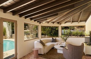 A sunlit patio with a white sofa, a round table, and a chair.
