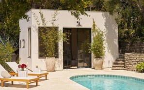 A modern outdoor pool area with a small building, lounge chairs, and potted plants.