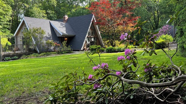 Une maison avec un toit en pente, entourée d’une pelouse bien entretenue et de divers arbres.