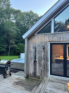 Une terrasse moderne en bois, dotée d’un jacuzzi, d’un barbecue et d’un espace salon extérieur.