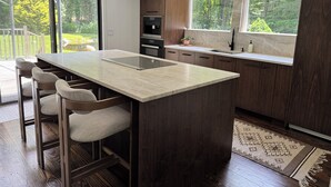 Une cuisine moderne dotée d’un grand îlot central, de tabourets de bar, d’un four encastré et offrant une vue sur l’extérieur.