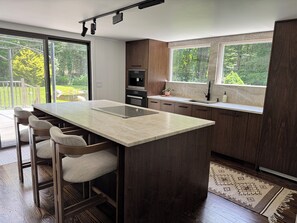 A modern kitchen with a large island, bar stools, a built-in oven, and a view of the outdoors. - Luxury Cabin for 6 - Stream - Pond - Custom Kitchen (Redding)