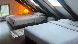 Une chambre mansardée avec un plafond en pente, deux lits, une table de chevet et une fenêtre laissant entrer la lumière naturelle.
