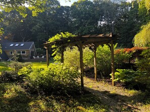 A wooden pergola in a garden with a house in the background.