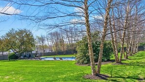 Ein Garten mit Swimmingpool, Bäumen und einem gepflegten Rasen.