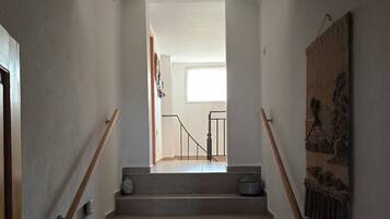 A staircase with wooden handrails, a light fixture above, and a textured wall on the right.