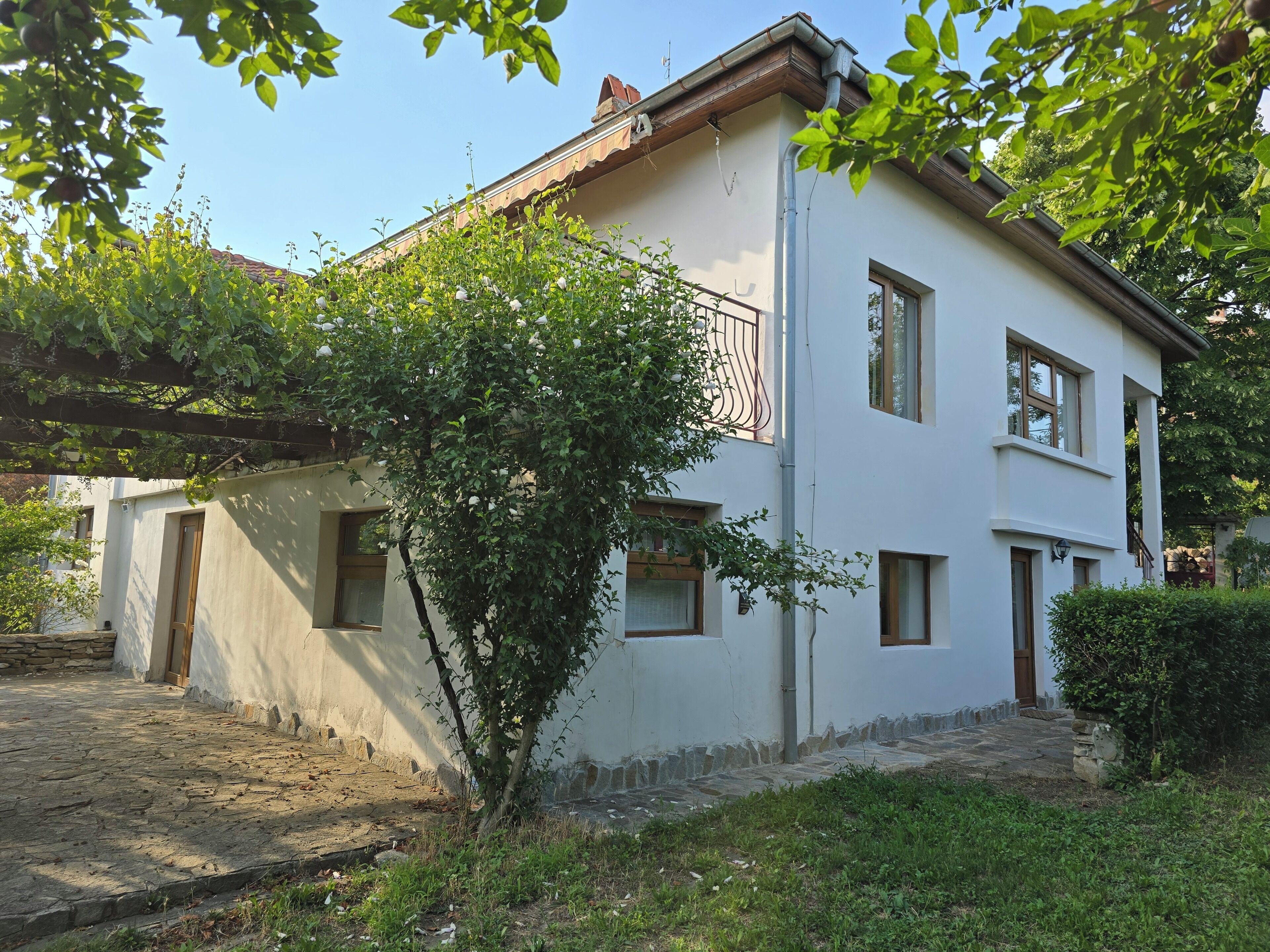 A two-story building with a stone-paved courtyard, a wooden door, and a small garden area.