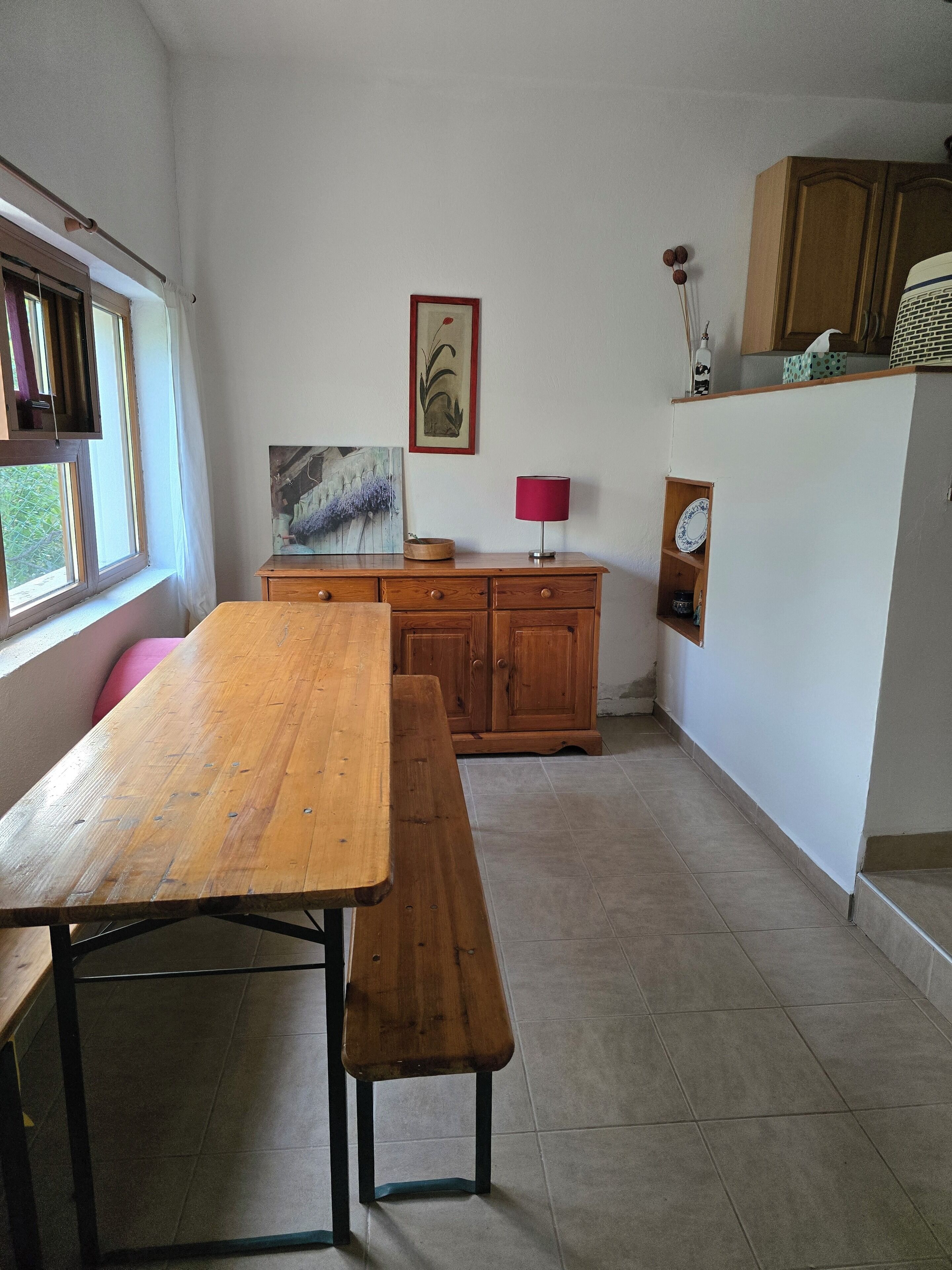 A room with a wooden table and bench, a cabinet, a framed picture, and a lamp.