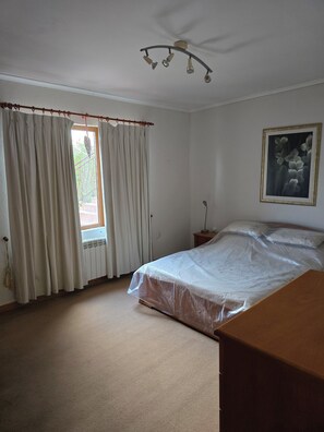 A bedroom with a bed, a window with curtains, a ceiling fan, and a framed picture on the wall.