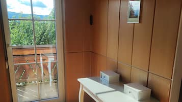 Ein Zimmer mit einer Schiebeglastür, die auf einen Balkon führt, einem weißen Tisch mit Schubladen und einem gerahmten Bild an der Wand.