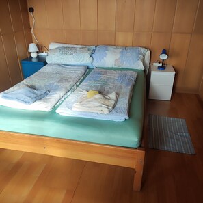 Een bed met een groene matras, meerdere kussens en een nachtkastje in het blauw met een lamp.