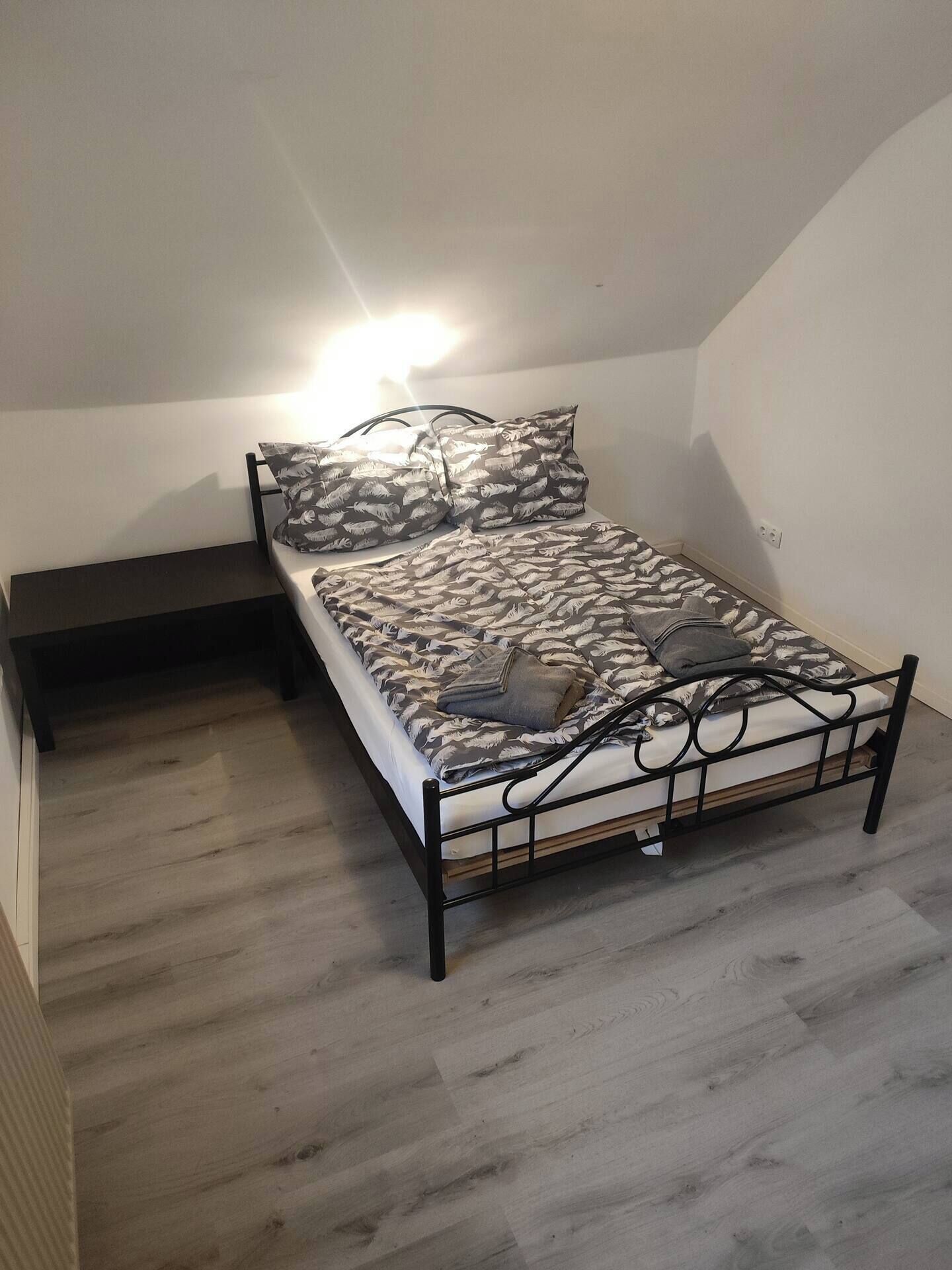A single bed with a patterned bedspread, a bedside table, and a wall-mounted light fixture.