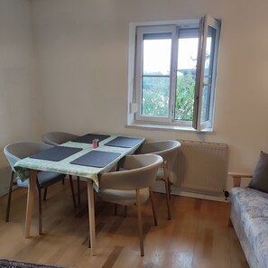 Une pièce comprenant une table à manger, des chaises, un radiateur et une fenêtre donnant sur un espace verdoyant.