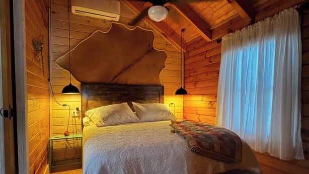 A cozy wooden cabin bedroom with a bed, a bench, a ceiling fan, and two bedside lamps. - Tranquil Cabin In Charming Bean Station Tn on Cherokee Lake With Boat Ramp (Bean Station)