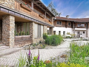 A two-story log cabin with stone walls and a balcony with red flowers.