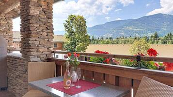 A balcony with stone pillars, wicker furniture, and a table with a bottle and glasses.