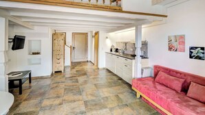 A spacious living area with a high ceiling, a kitchen with modern appliances, and a red sofa.