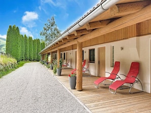 A wooden deck with red lounge chairs, a gravel path, and a row of potted plants.