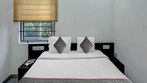 A hotel room with a bed, a window with a view, a bedside table, and an air conditioning unit. - Hotel O Thrissur Railway Junction (Thrissur)