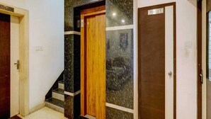 A hallway with a wooden door, a marble wall, and a sign indicating a toilet. - Hotel O Thrissur Railway Junction (Thrissur)