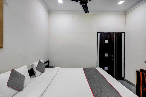 A hotel room with a bed, pillows, a wardrobe, and a ceiling fan.