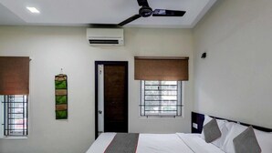 Habitación de hotel con cama, ventilador de techo, aire acondicionado y ventanas con persianas.