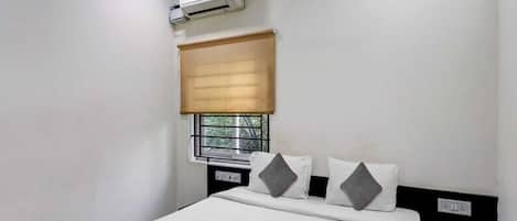 Une chambre d’hôtel comprenant un lit, un ventilateur de plafond, un appareil de climatisation, une fenêtre avec un store et une table de chevet.