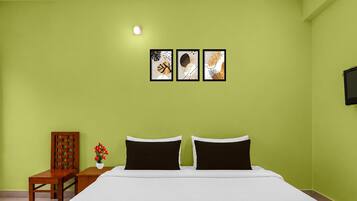 A bedroom with a bed, a chair, a small table with a vase of flowers, and three framed pictures on the wall.