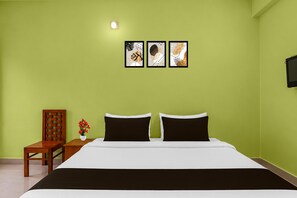 A bedroom with a bed, a chair, a small table with a vase of flowers, and three framed pictures on the wall.