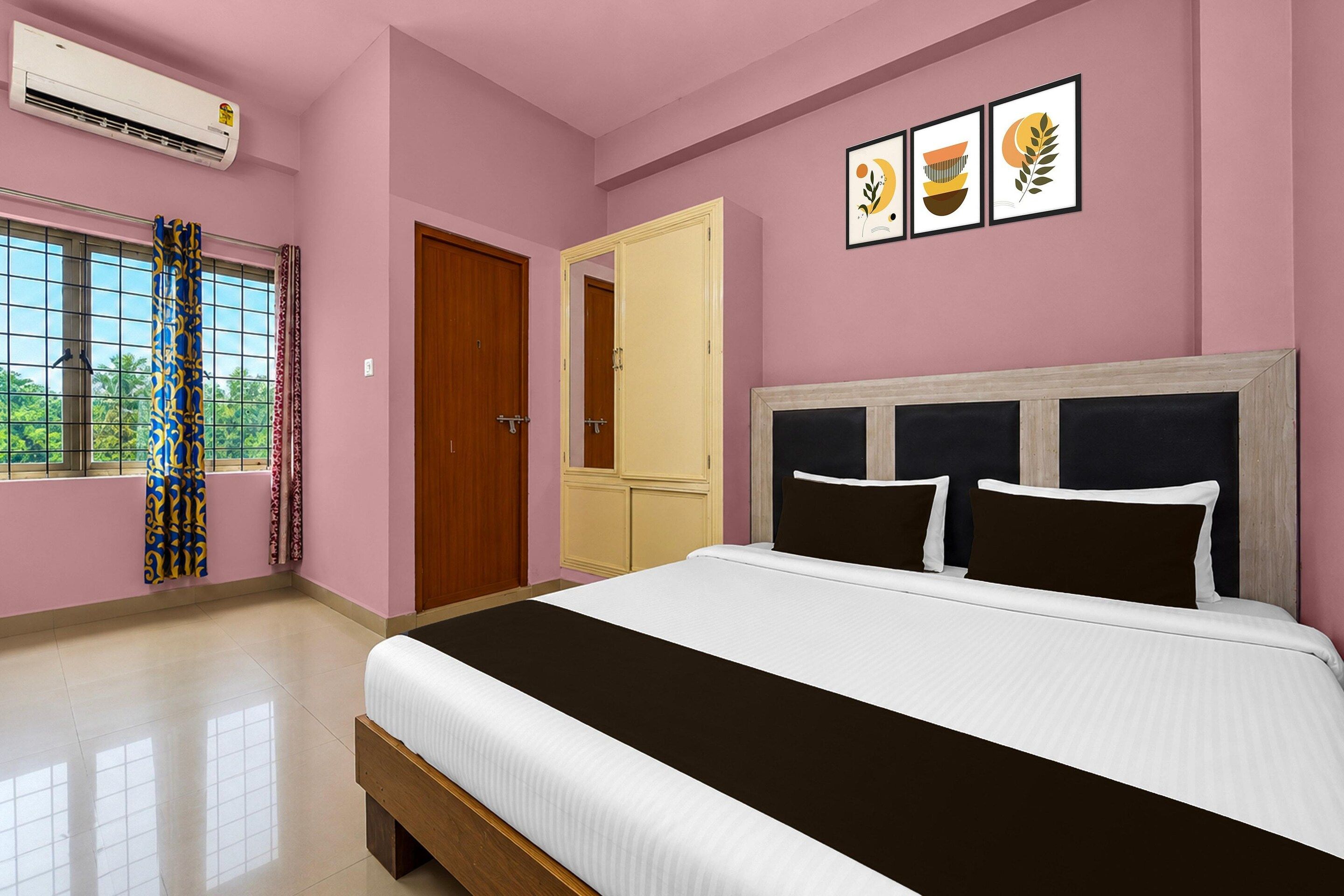 A bedroom with a bed, a wardrobe, a window with curtains, and a wall with framed artwork.