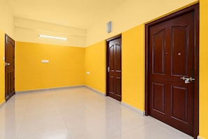 A hallway with yellow walls and a tiled floor, featuring two wooden doors and a ceiling light fixture.