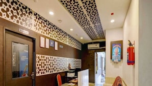 A reception area with a patterned wall, a reception desk, a chair, a sofa, and a fire extinguisher. - Hotel O Thrissur Railway Junction (Thrissur)