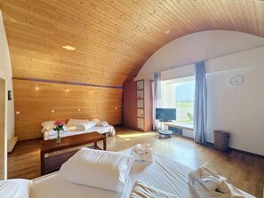 A room with wooden ceiling, a bed, a TV, and a window with curtains.