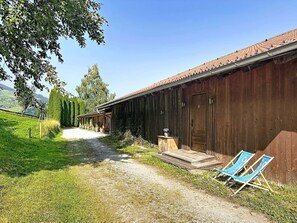 A rustic wooden building with a gravel path leading to a wooden door. There are two blue chairs outside.