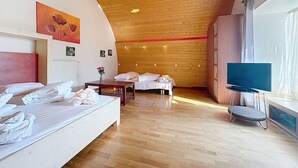 Quarto de hotel com teto de madeira, cama, escrivaninha, cadeira, televisão e janela.