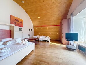 Ein Hotelzimmer mit Holzbalkendecke, einem Bett, einem Schreibtisch, einem Stuhl, einem Fernseher und einem Fenster.