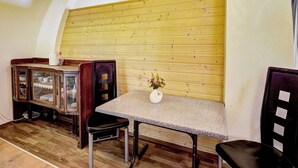 Um quarto com parede de madeira, uma mesa com cadeiras, um armário com portas de vidro e um vaso com flores.