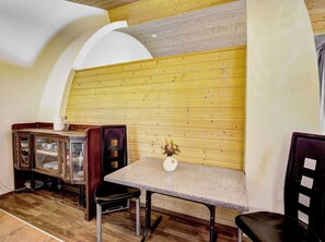 Ein Zimmer mit Holzwand, einem Tisch mit Stühlen, einem Schrank mit Glastüren und einer Vase mit Blumen.