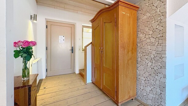 Um corredor com piso de madeira, um guarda-roupa de madeira, um vaso com flores e uma parede de pedra.