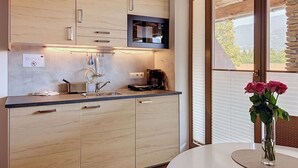 Uma cozinha moderna com armários de madeira, micro-ondas embutido e um espaço de jantar com mesa e vaso de flores.