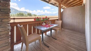 Um deck de madeira com mesa e cadeiras, com vista para uma paisagem montanhosa.