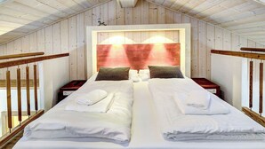 Uma cama de casal com lençóis e toalhas brancos, uma cabeceira de madeira e duas mesas de cabeceira com abajures.