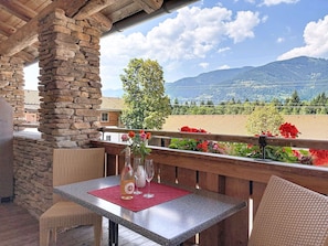 Ein Balkon mit Steinsäulen, Korbmöbeln und einem Tisch mit Flasche und Gläsern.