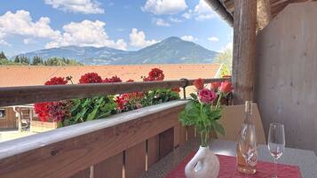 A balcony with a wooden railing, a vase with flowers, and two wine glasses on a table.