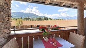 Ein Holzbalkon mit Tisch und Stühlen, der einen schönen Ausblick auf eine Landschaft mit Bergen und Feldern bietet.