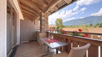 A wooden balcony with a table and chairs, overlooking a mountainous landscape.