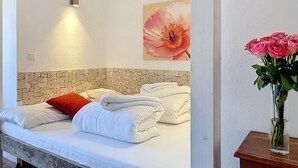 Ein Hotelzimmer mit einem Bett, weißen Handtüchern, einem roten Kopfkissen, einem Kopfschild mit Steinmuster, einer Wandleuchte und einem Blumenbild.