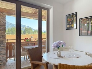 A room with a round table, wicker chairs, a vase with flowers, and two framed botanical prints on the wall.